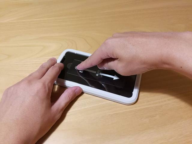 iPhone 11 Pro Maxにガラスフィルムを貼り付け、指で押さえている画像